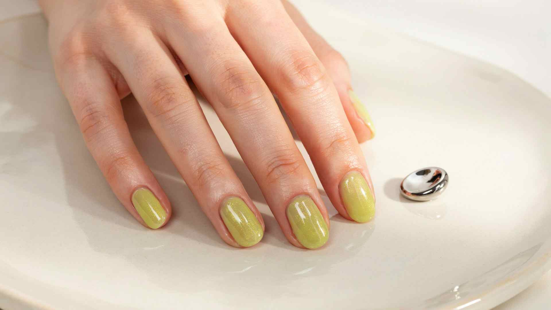 Chartreuse cat eye nails with narrow magnetic light bands floating through glossy yellow green polish on almond tips