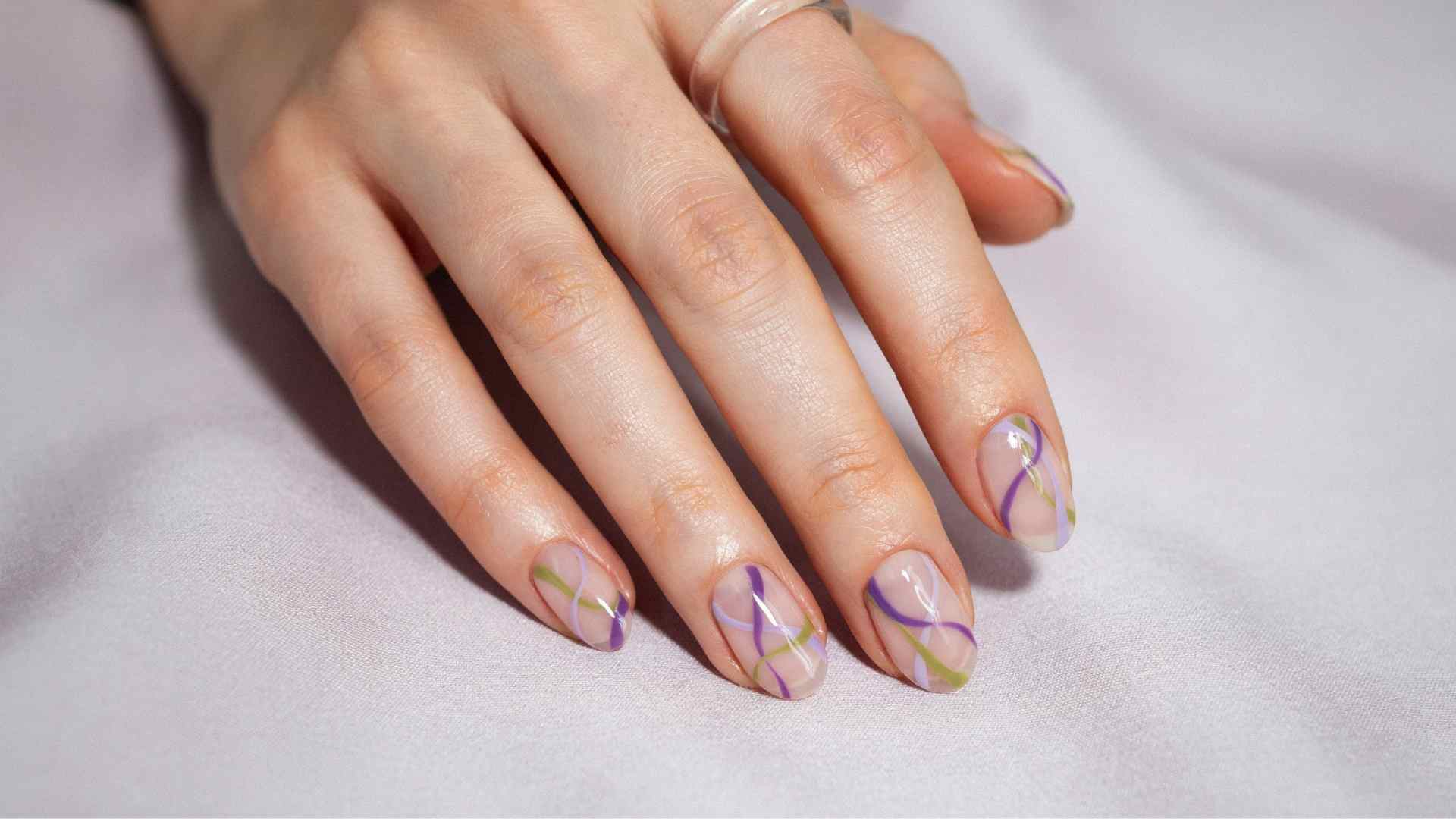 Purple and lime swirl lines move across medium ballerina nails with a sheer base and soft lilac satin background