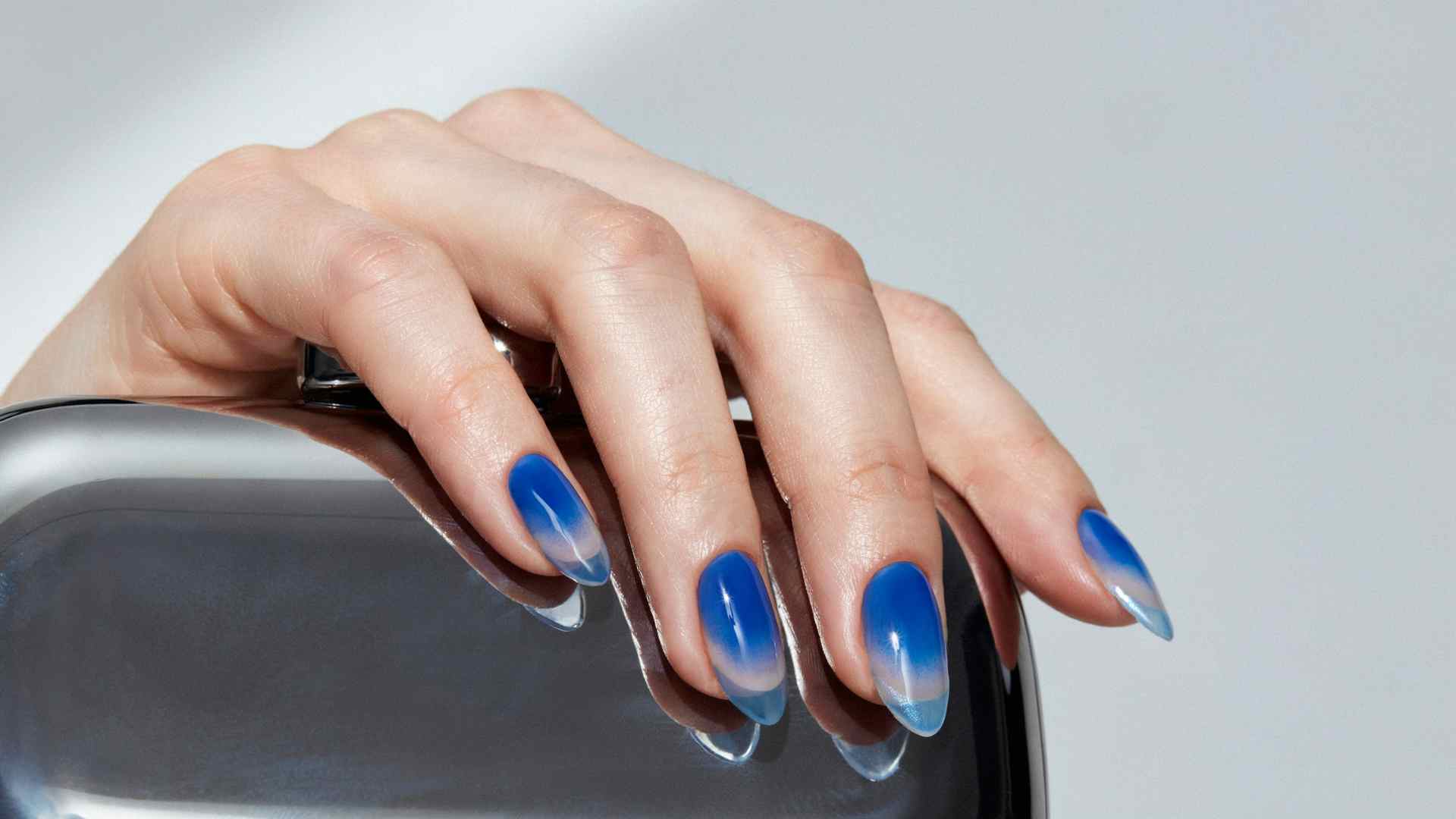 Electric blue chrome aura nails fade toward icy edges on long stiletto tips with fragmented metallic reflections