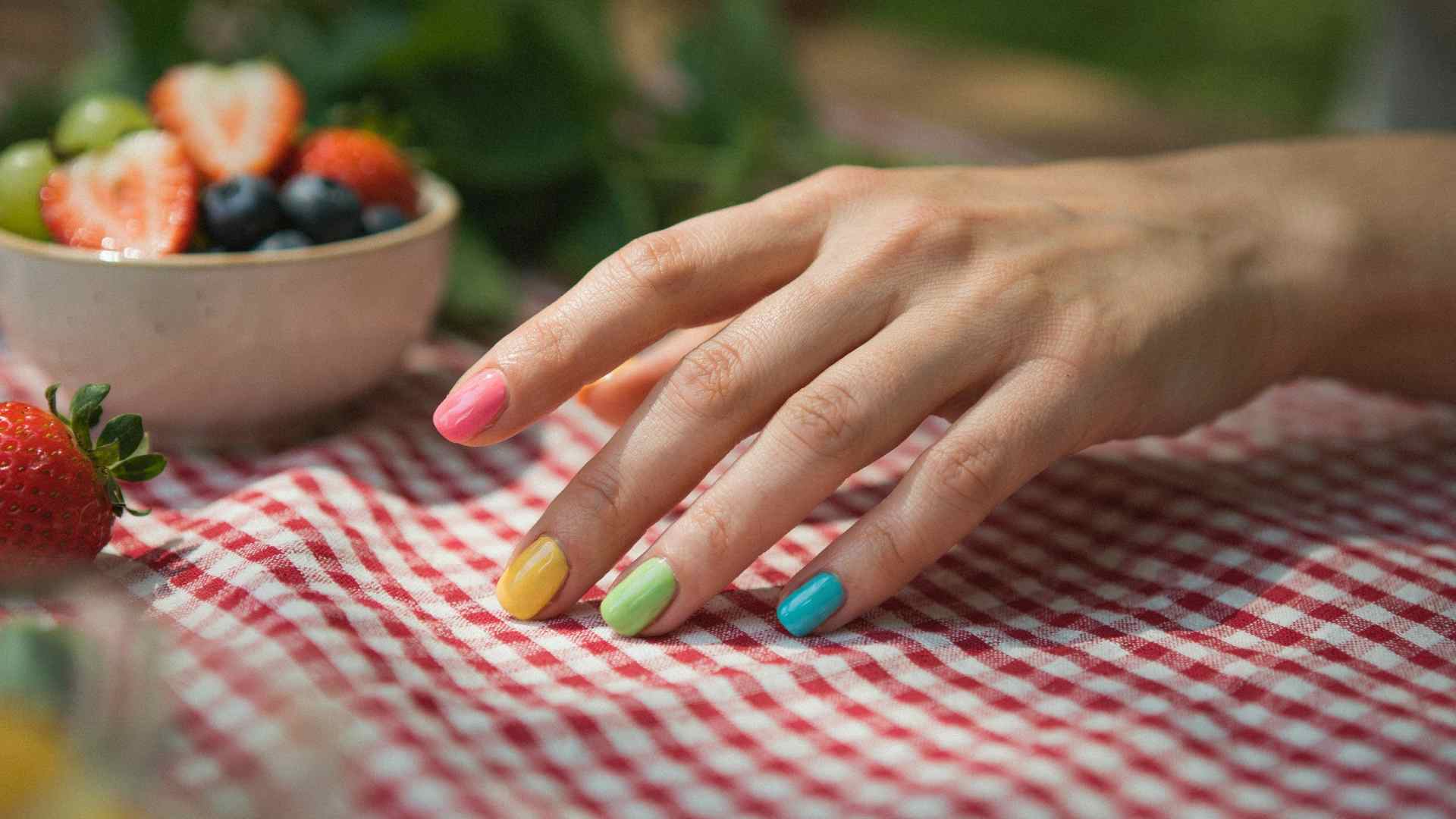 Short rounded Skittle nails feature pink orange yellow lime and turquoise polish in a casual summer picnic setting