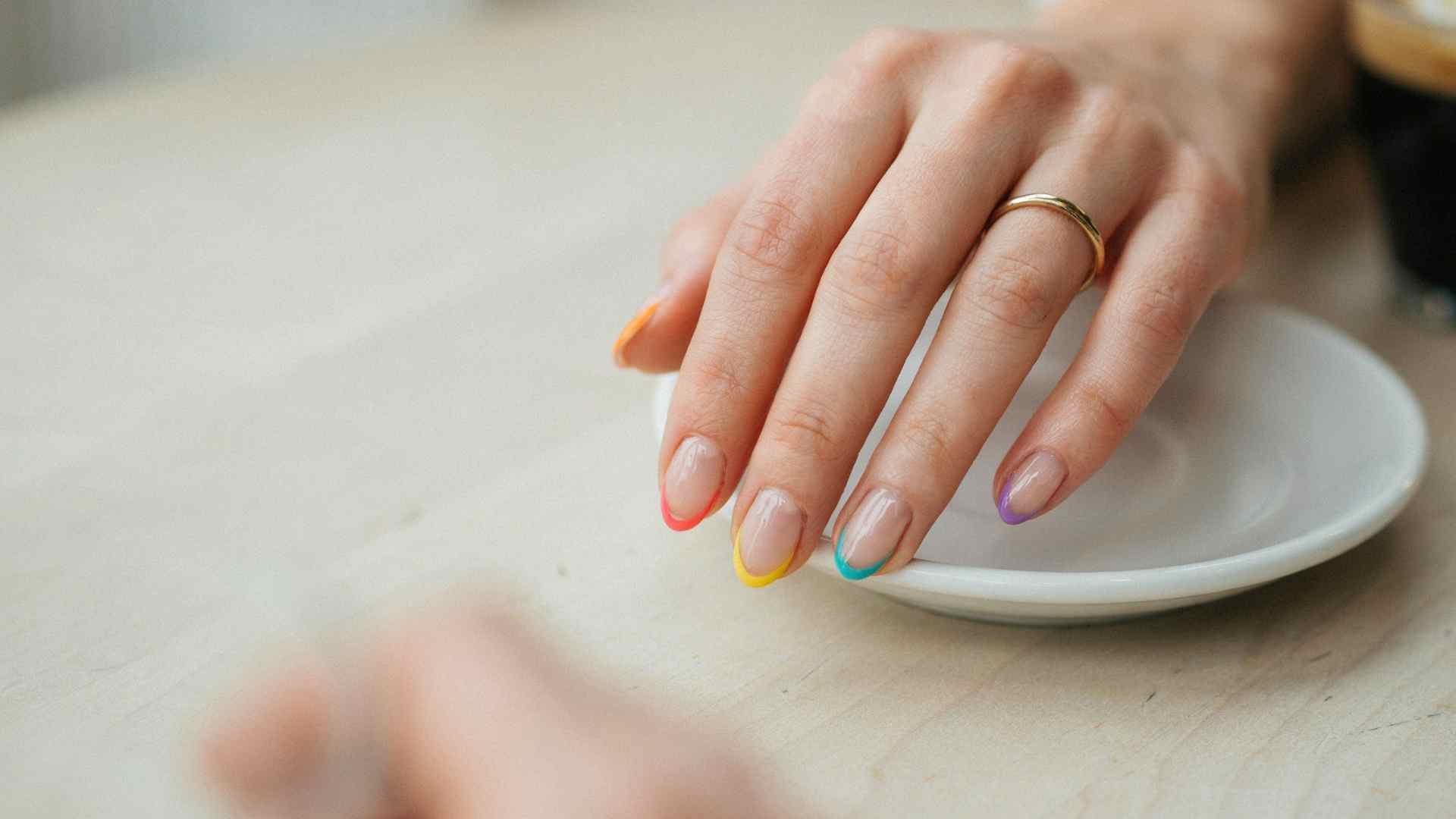 Rainbow neon French tips trace medium oval nails with a sheer base and different bright colors along every edge