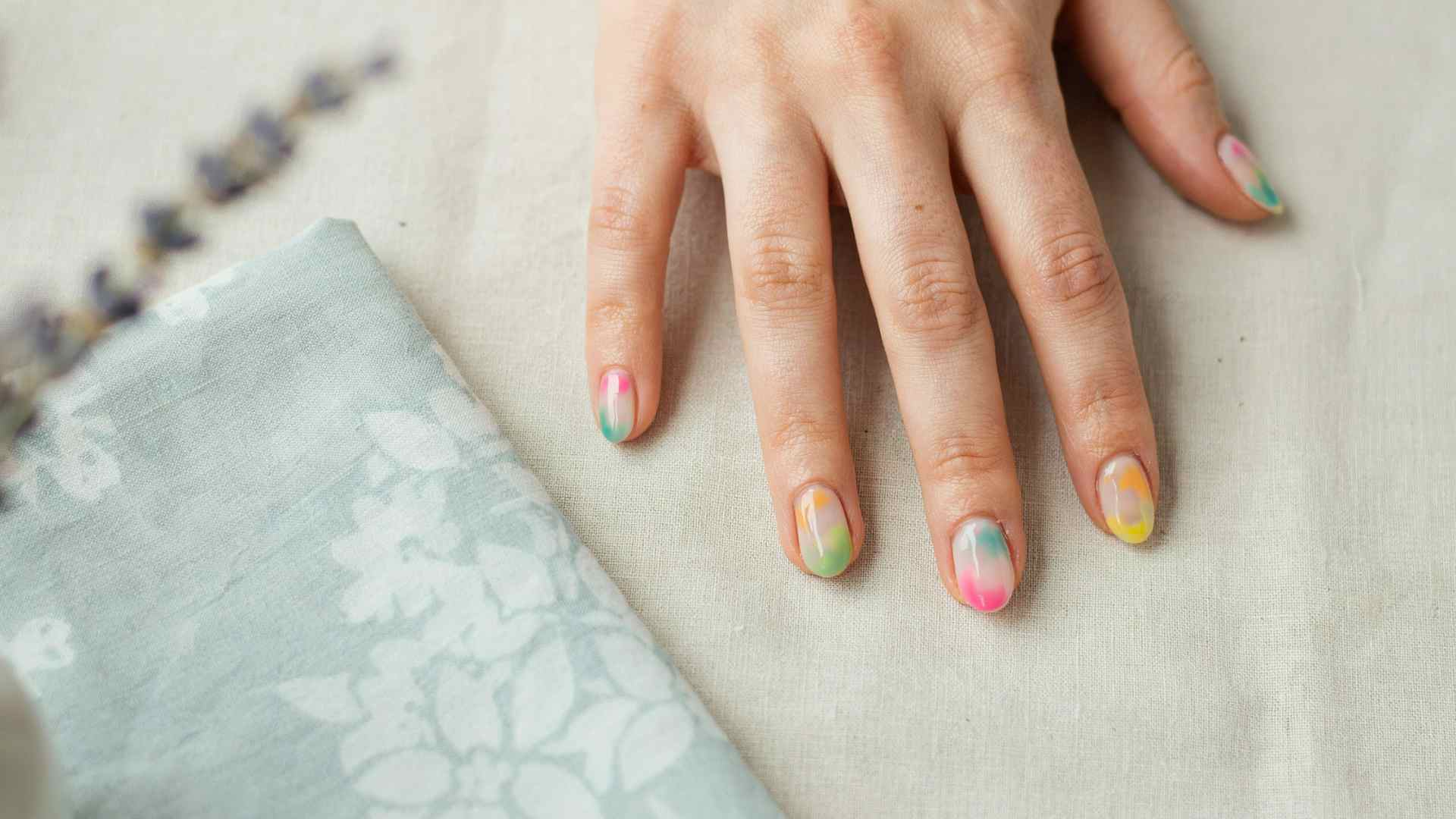 Neon tie dye nails blend pink orange yellow lime and aqua across medium oval tips with soft translucent color