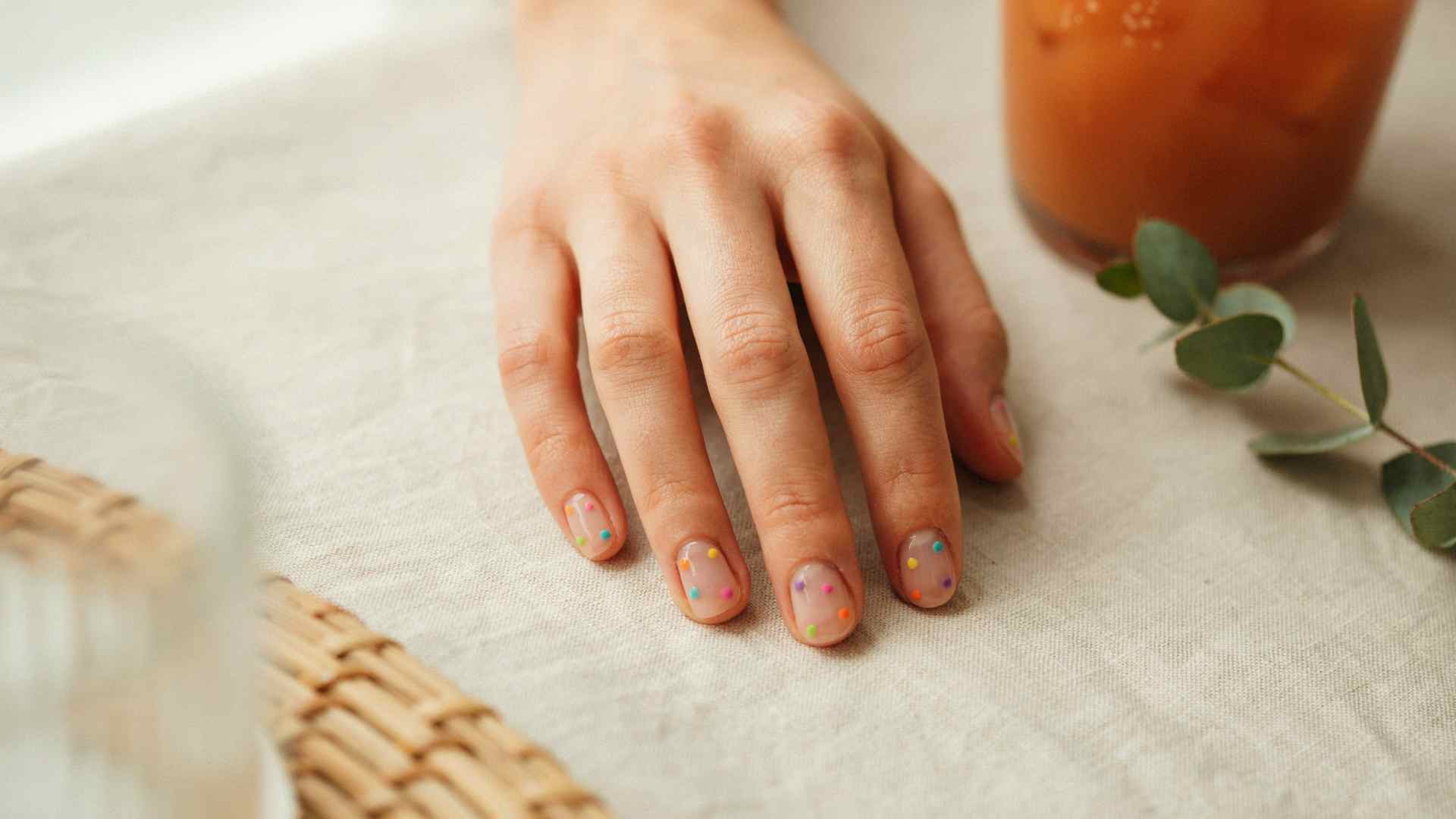 Rainbow neon dots scatter across short squoval nails with a sheer blush base and plenty of natural nail visible
