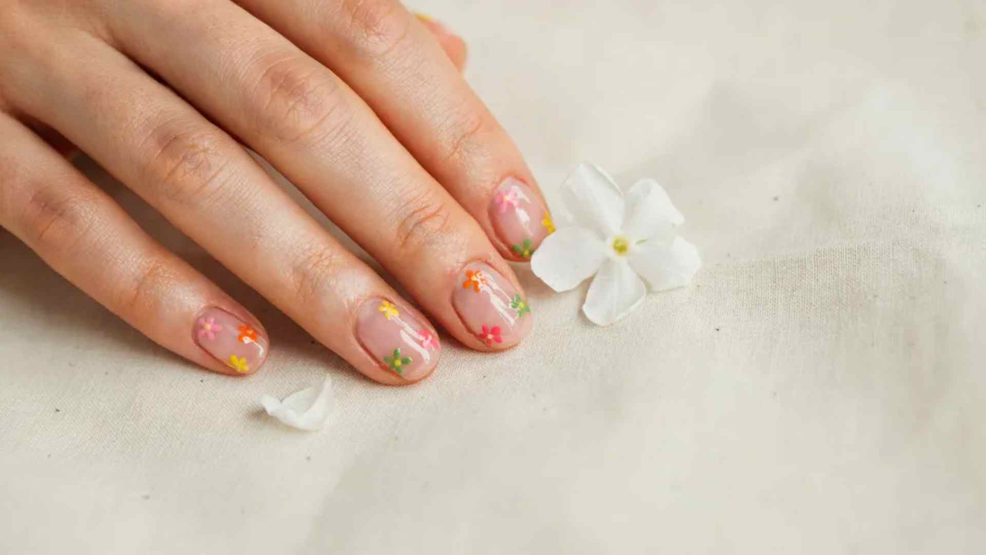 Tiny neon flowers decorate medium rounded nails with a sheer nude base and generous open space between floral details