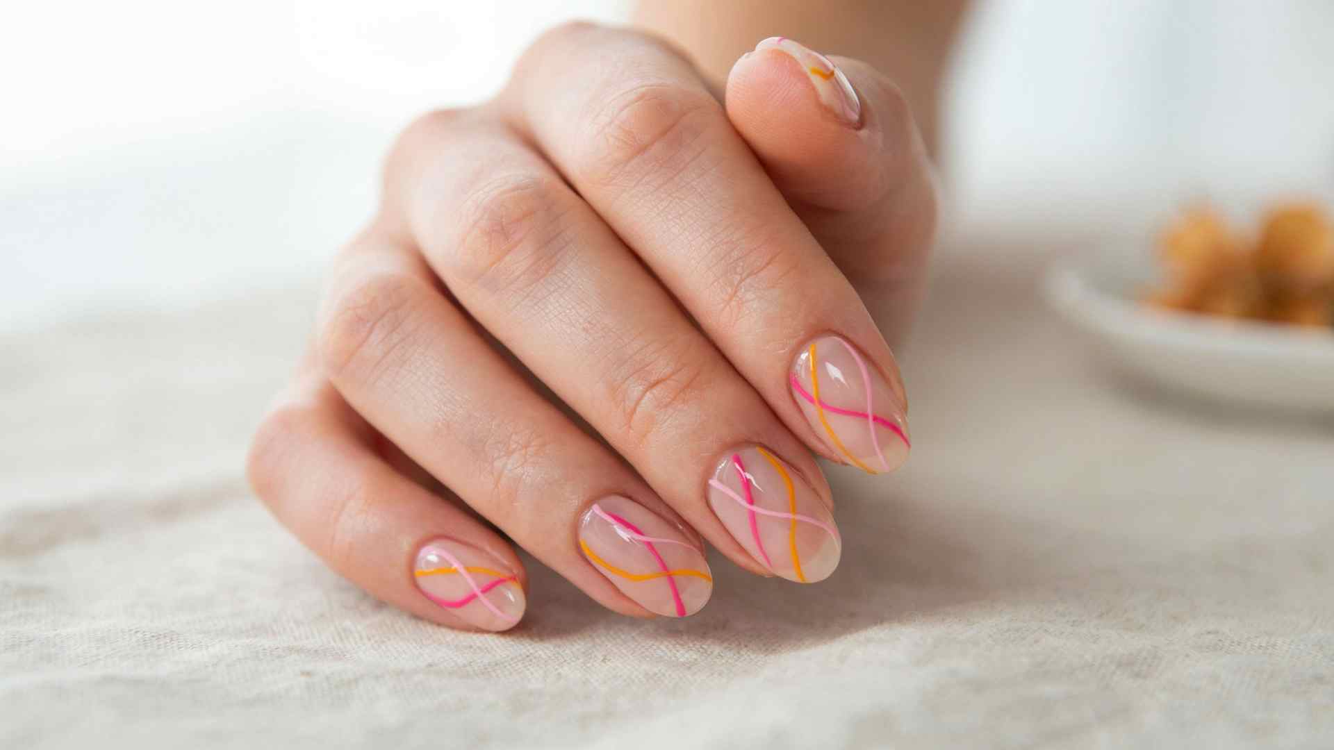 Neon pink and orange swirl nails with curved artwork over a nude base creating a bright summer manicure style