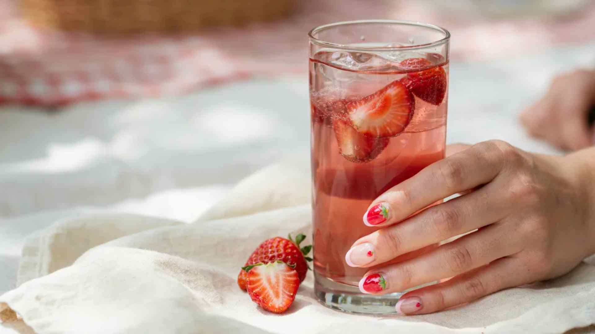 Tiny neon strawberries decorate short rounded nails with a sheer pink base and fine fruit details for summer