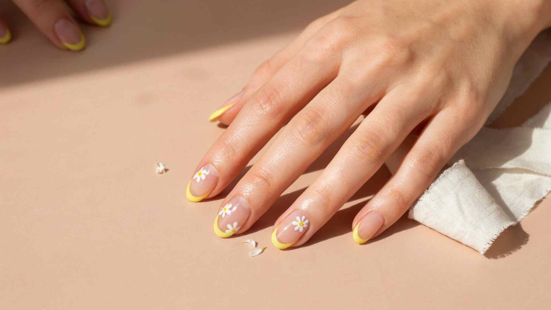 Neon yellow tips and tiny white daisies decorate medium squoval nails with a sheer nude base in summer light