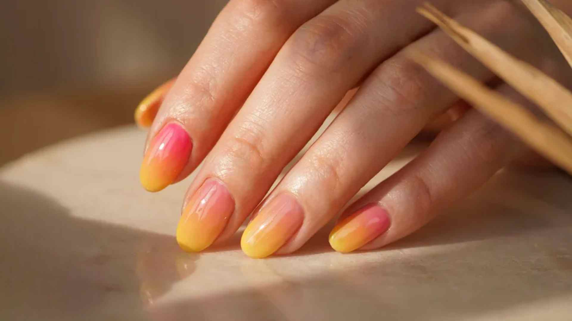 Pink orange and yellow sunset ombre nails blending neon shades with a glossy summer manicure finish