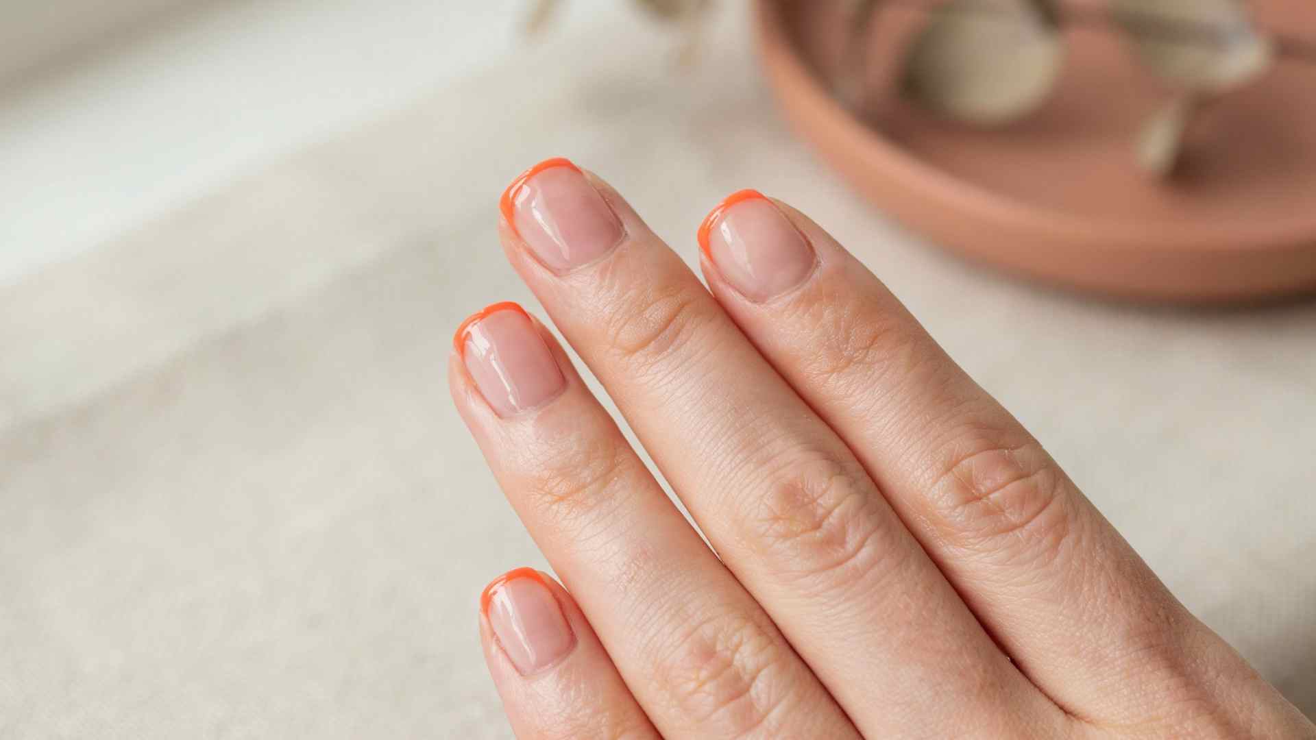 Neon orange micro French tip nails with thin bright lines over a sheer nude summer manicure base