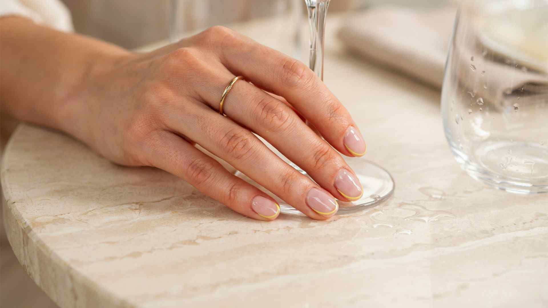 Neon yellow micro French tips over a sheer pink base on short natural nails photographed in soft summer café light
