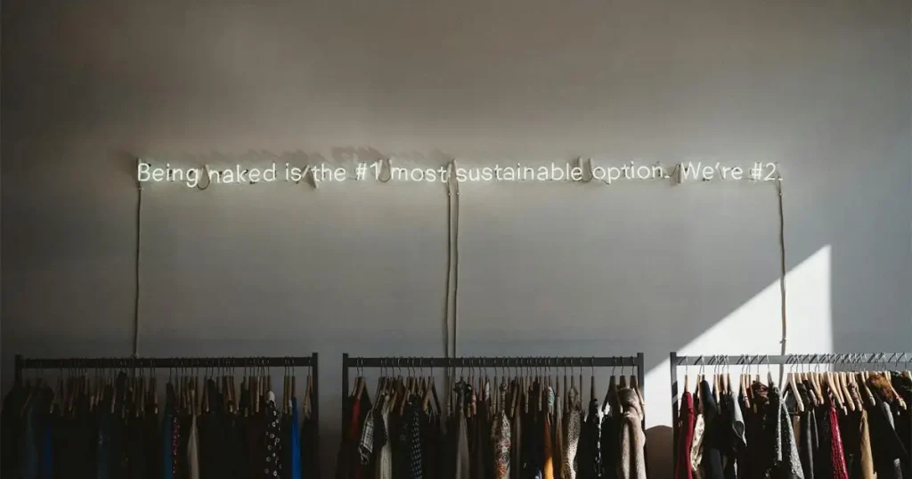 Clothing racks under neon sustainability sign in a retail store setting