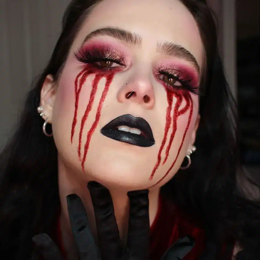 Bloody shadow makeup with red and black smoky eyes, fresh fake blood dripping below the lashline, and smudged edges