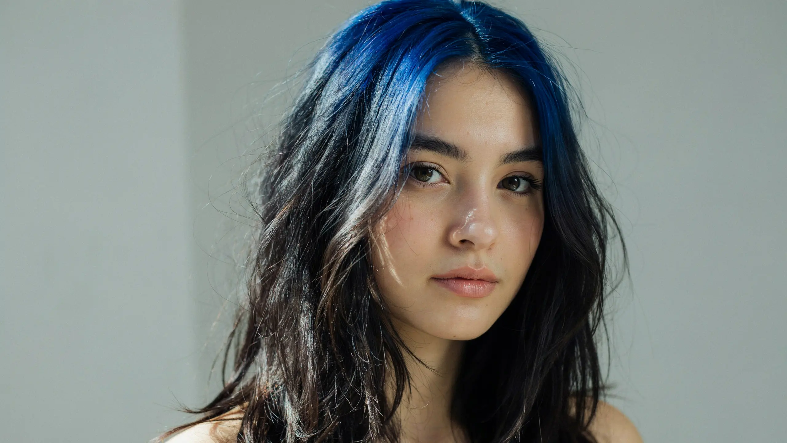 Black hair with vivid blue shadow roots blending softly from the scalp into dark lengths for a dimensional fashion color effect