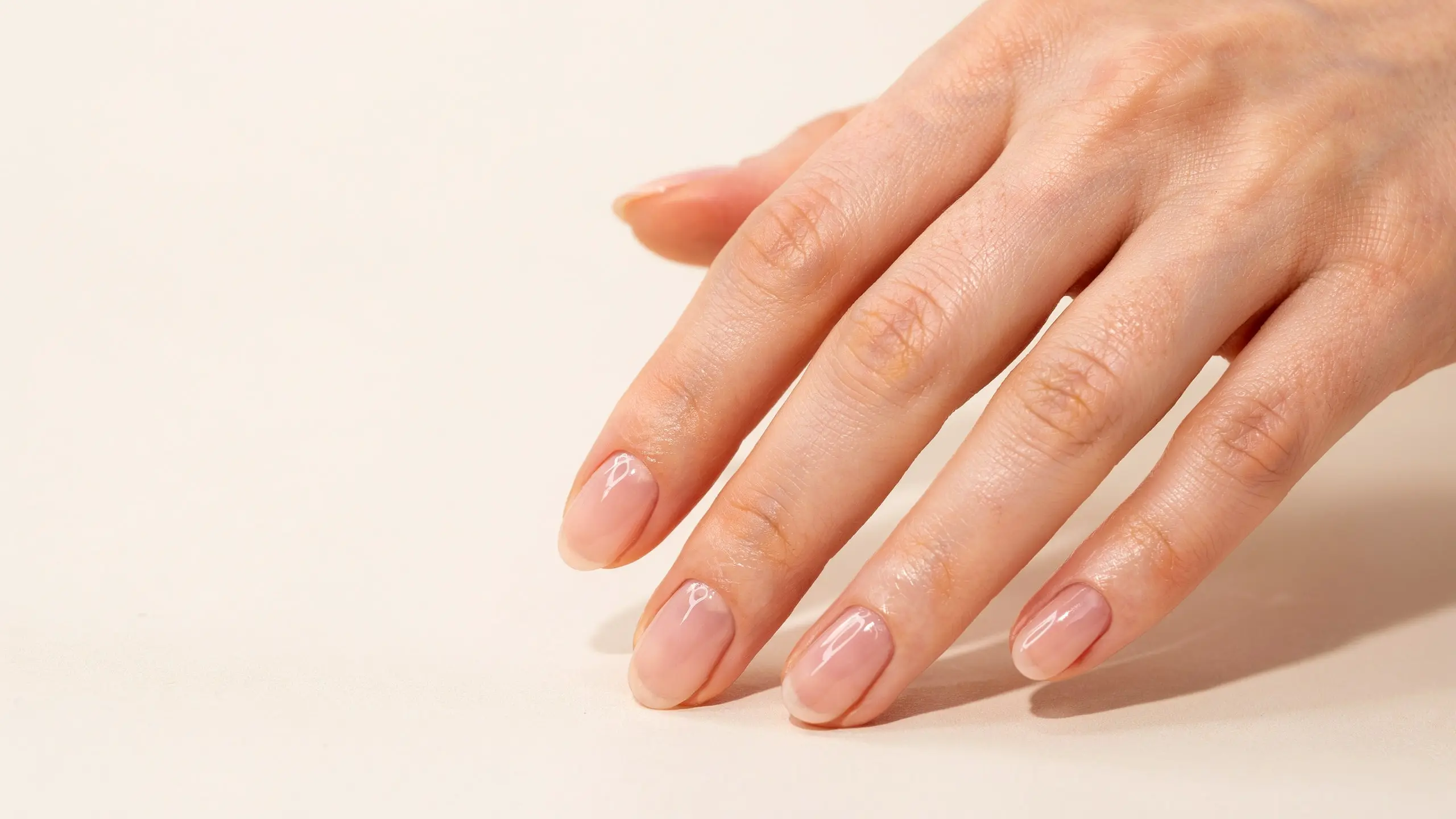 Close view of glossy blush pink nails on a hand resting against a soft cream background in warm natural afternoon lights
