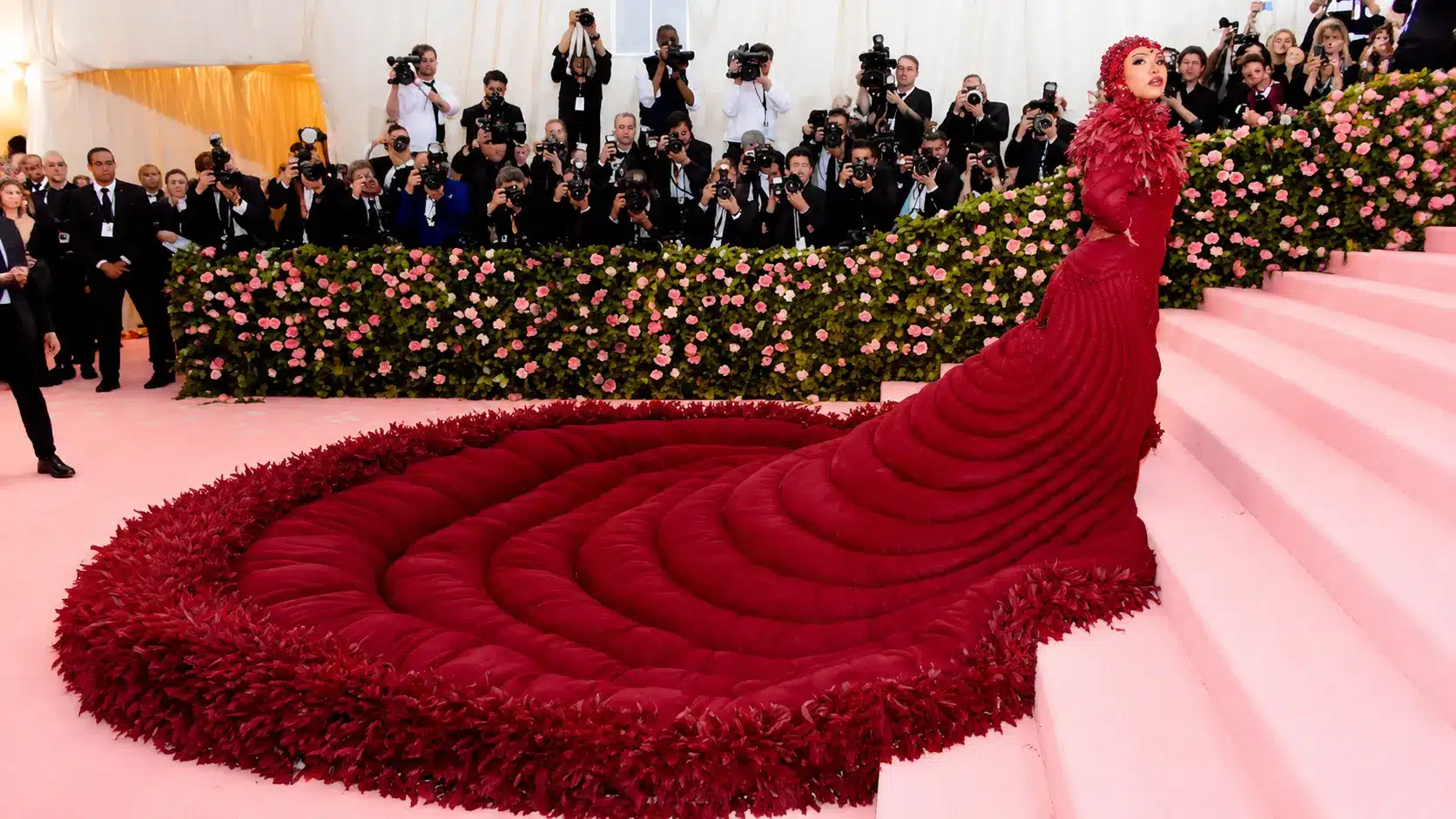 Camp fashion moment featuring Cardi B in a dramatic red feathered gown with an oversized train at the Met Gala