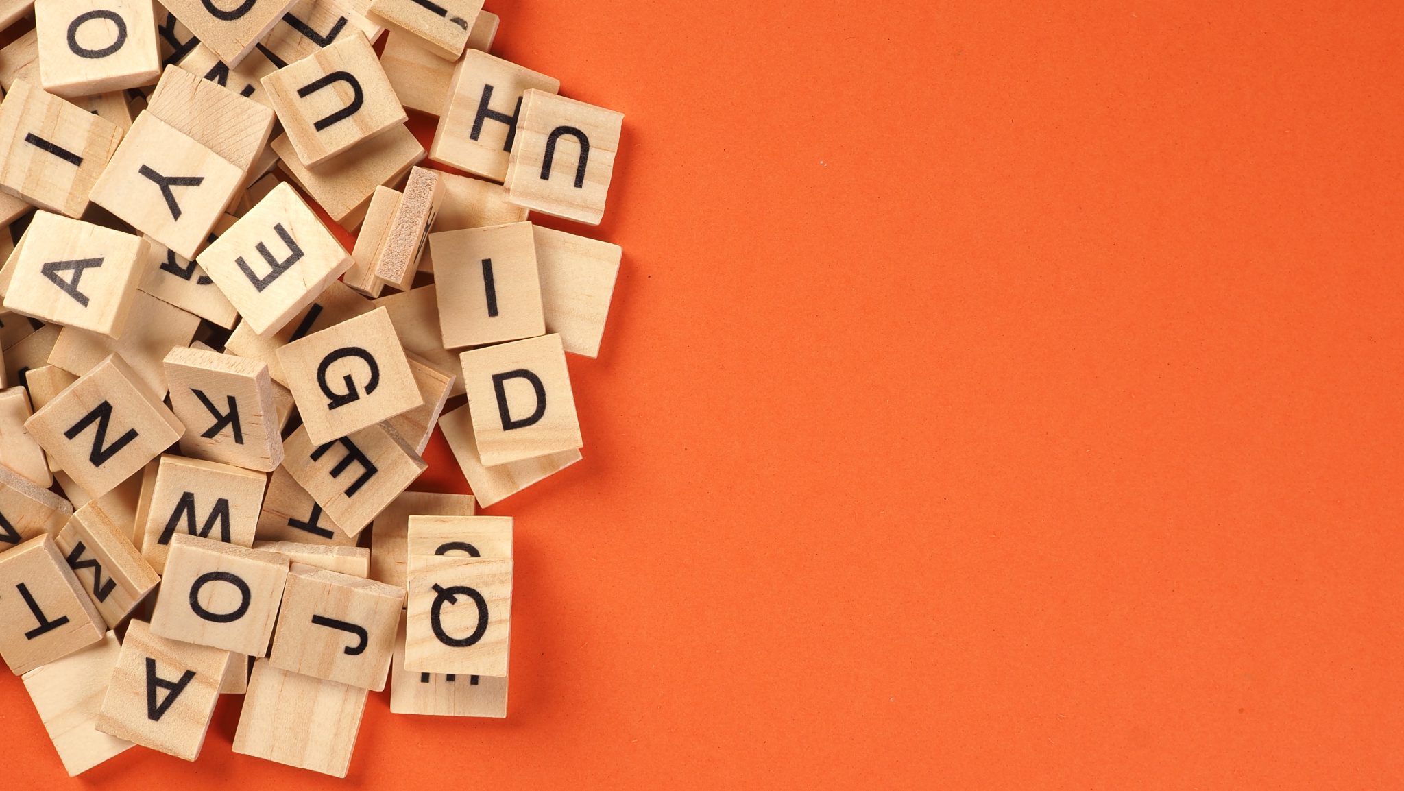 Wooden letter tiles scattered on orange background in a flat lay arrangement