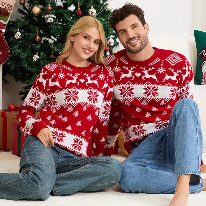Couple wearing matching red and white Christmas sweaters sitting by a decorated tree