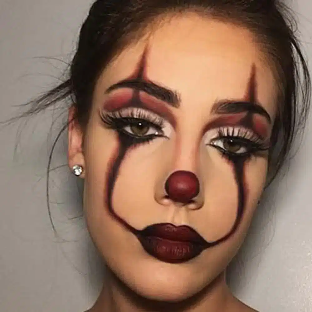 Creepy clown makeup with a white base, an oversized red mouth, downward black eye lines, and colorful cheek accents