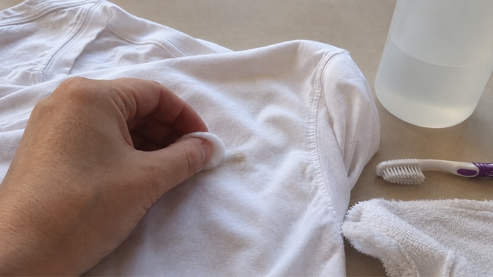 Fabric safe adhesive remover applied to an old nail glue stain on thick clothing material during cleaning