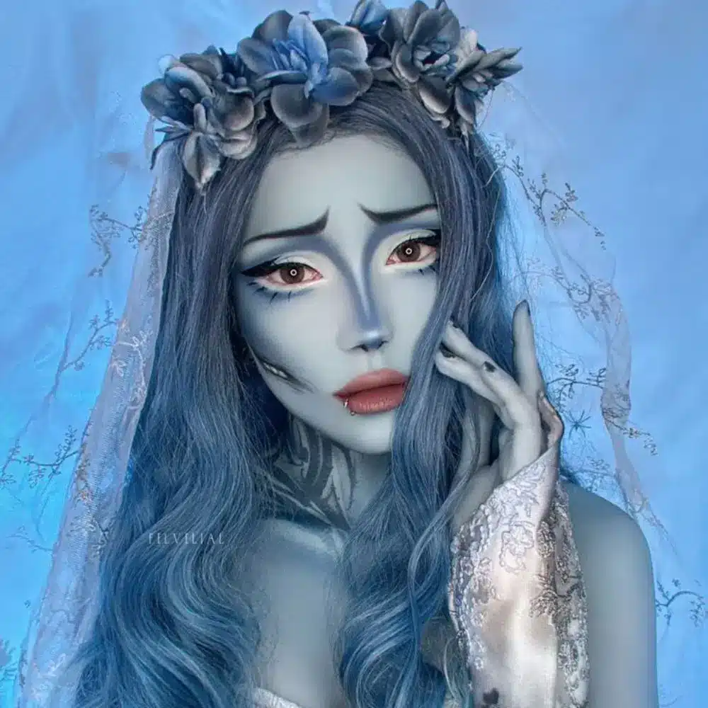 Corpse Bride makeup with pale blue skin, deep navy eye sockets, dark blue lips, and delicate black stitched details