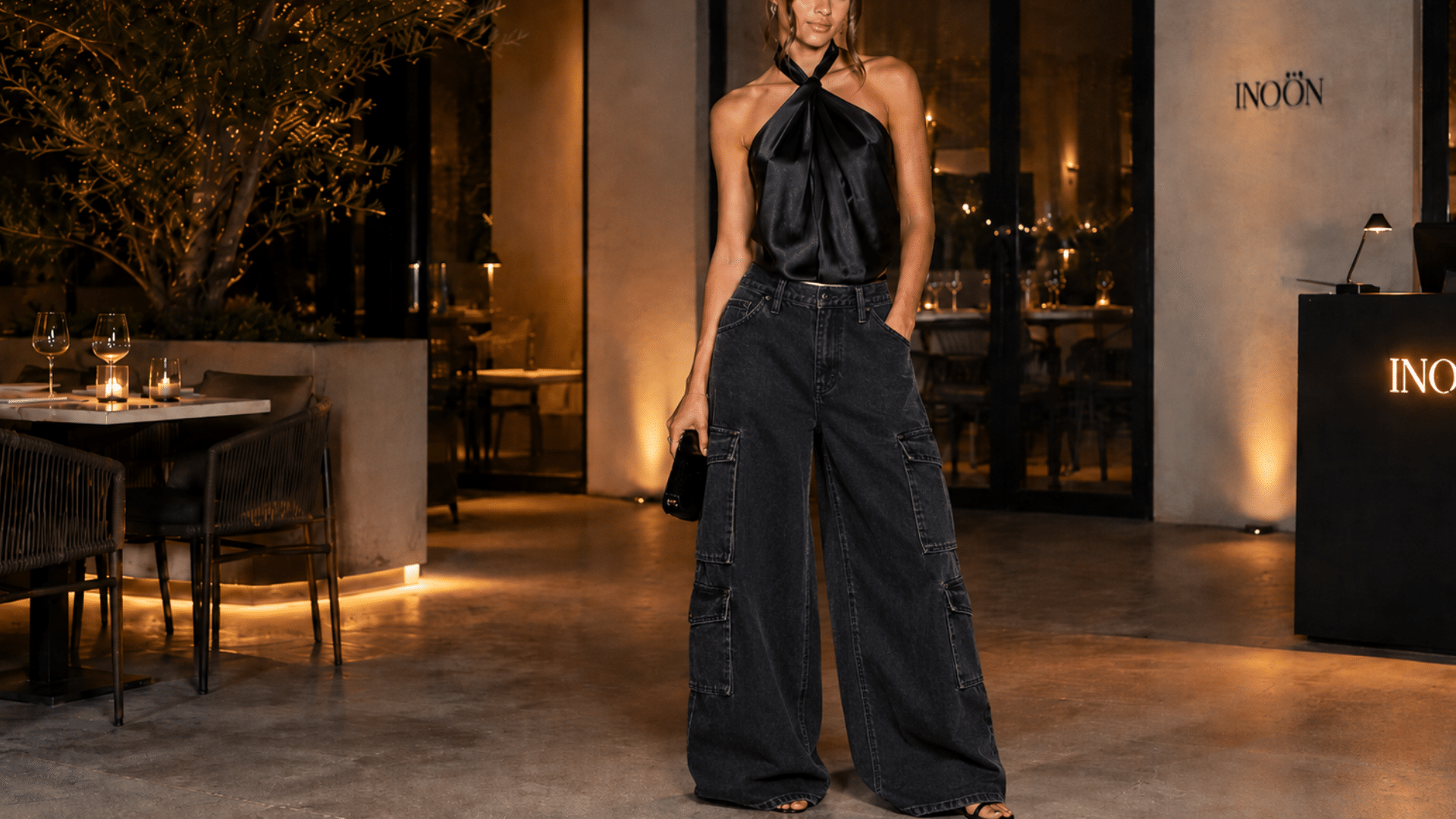 Woman wearing black satin cargo pants with fitted top and heels in a chic restaurant setting for evening fashion