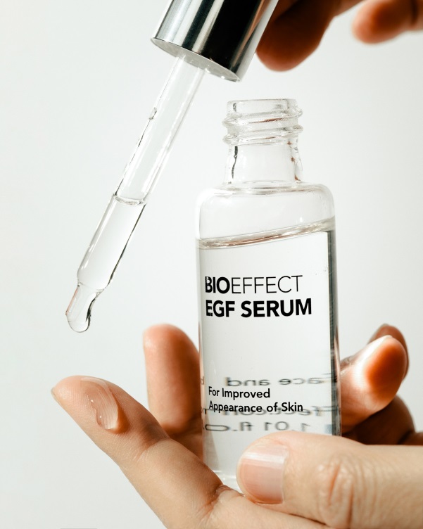 Dropper applying clear serum on fingertip from glass bottle in bright setting