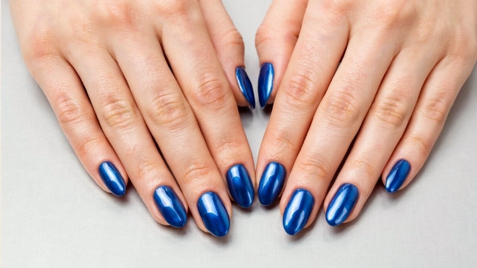 Electric blue chrome nails with a reflective metallic finish on long almond shaped nails for a futuristic look