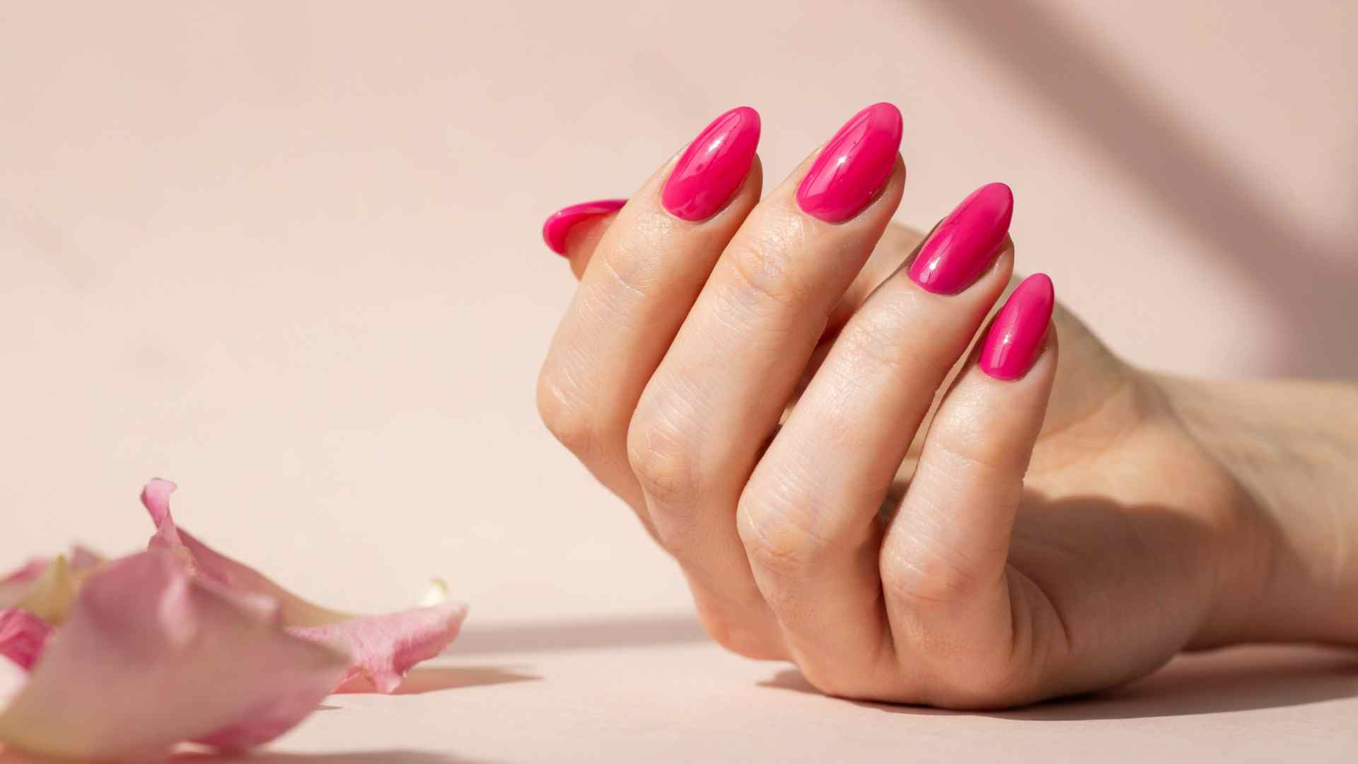 Electric pink glossy nails with a smooth summer manicure finish showing bright neon polish on almond shaped nails