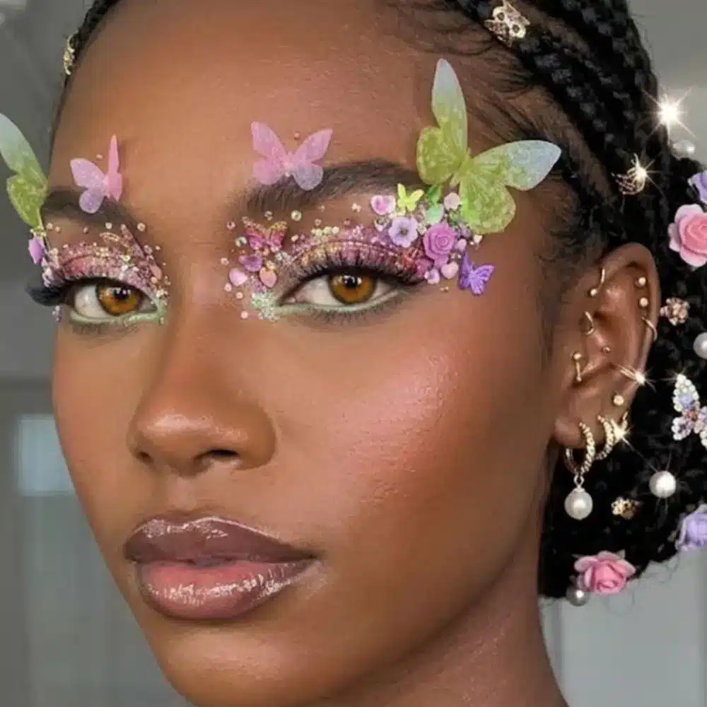Woodland fairy makeup with soft green and brown eyes, small wild flowers along the cheekbone, and glossy neutral lips