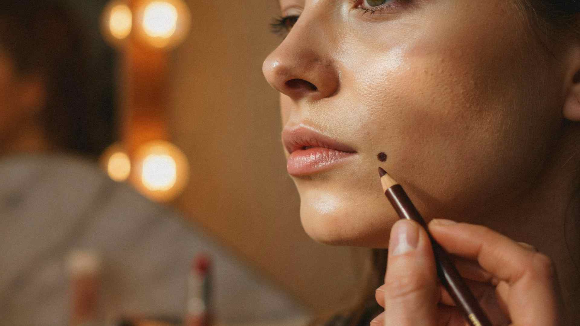 Applying a faux beauty mark with a cosmetic pencil near the lip