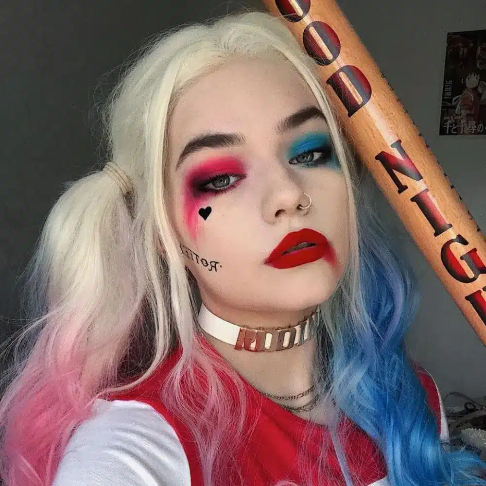 Harley Quinn makeup with a pale face, split red and blue eye colors, graphic black details, and bright red lipstick