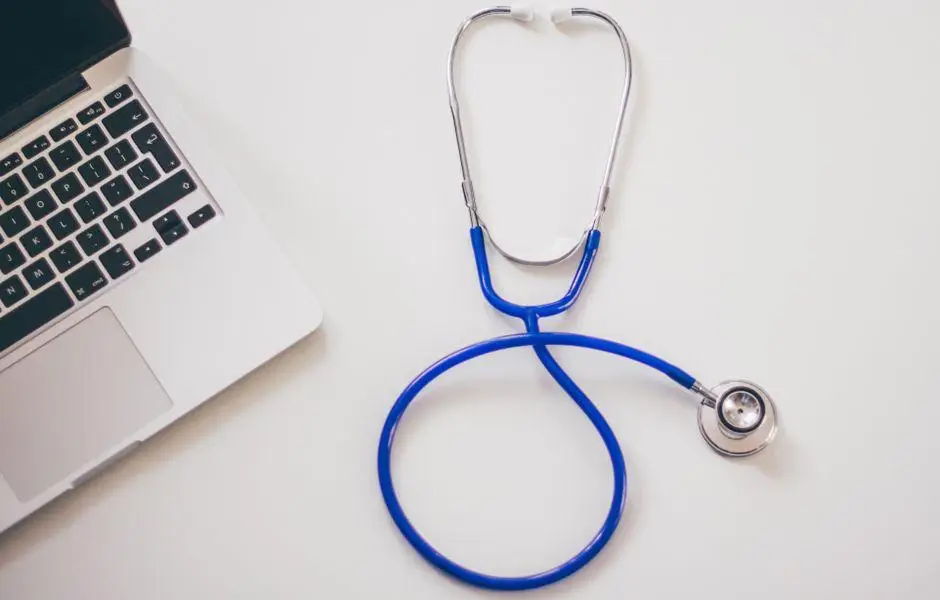 Open silver laptop beside blue stethoscope on white surface