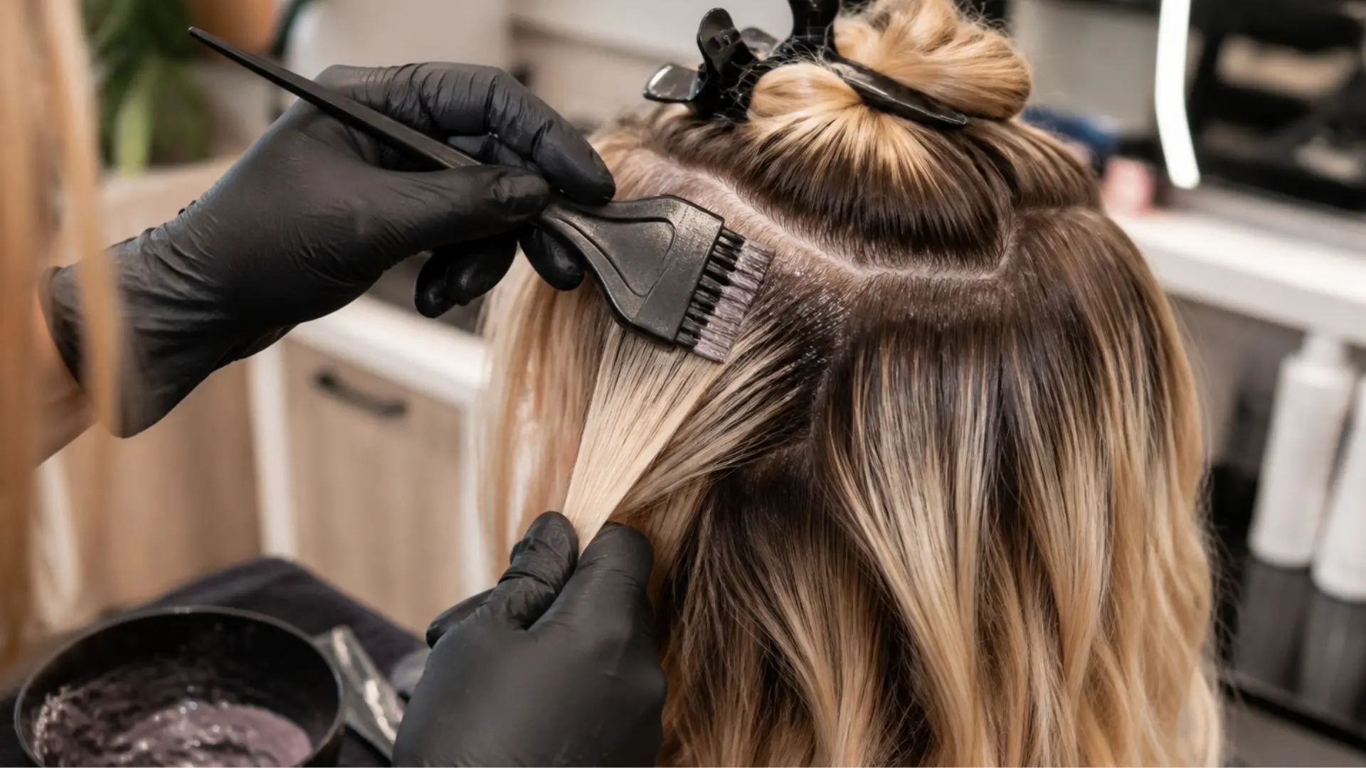 Hairstylist applying shadow root color with a brush to sectioned blonde hair during a professional coloring process