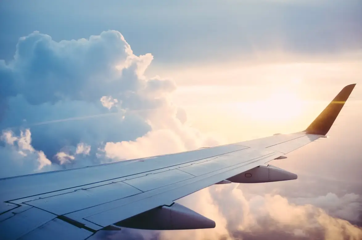 Airplane wing above clouds with sunset in the background