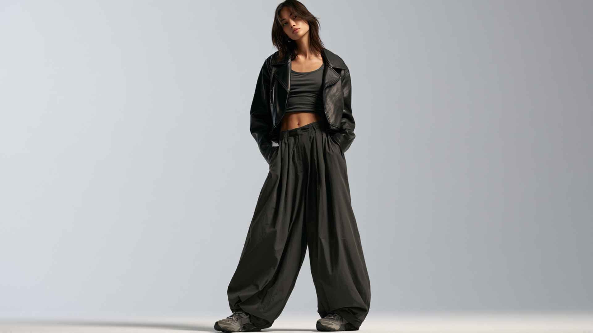 Woman styling wide-leg parachute pants with a cropped leather jacket and simple top for an edgy streetwear look.