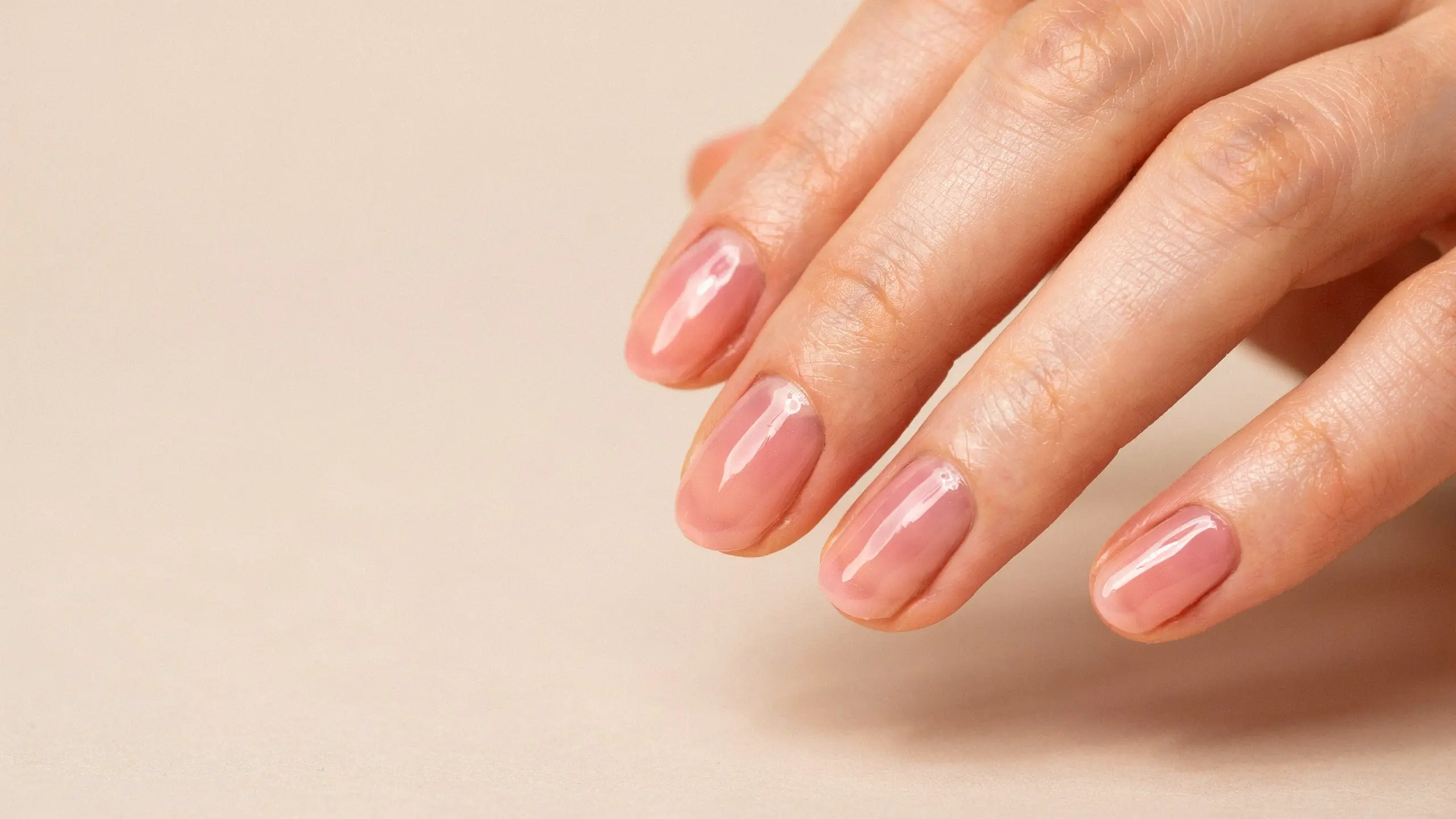 Close up of lip gloss nails featuring shiny sheer pink polish with a fresh natural manicure finish