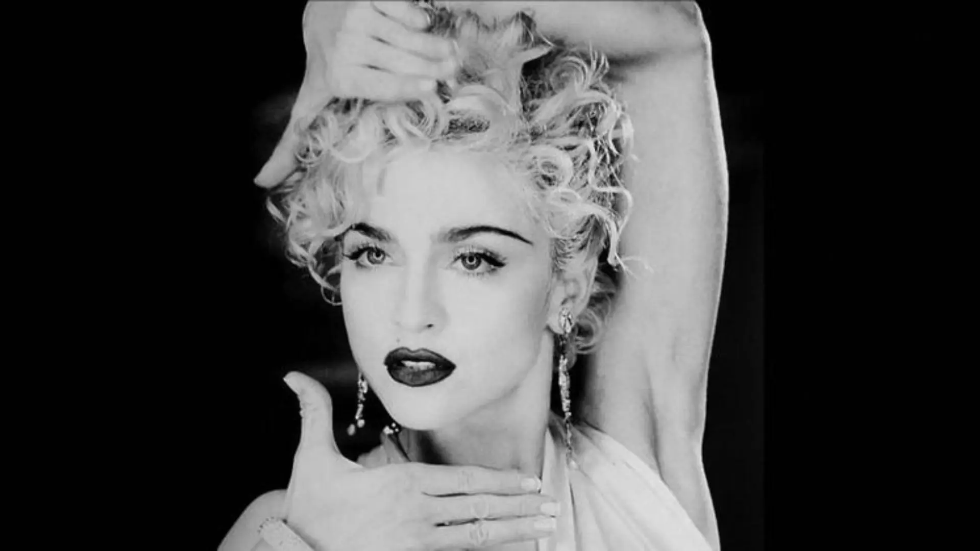 Retro black and white studio portrait of a woman posing with hands around her face and styled curly hair