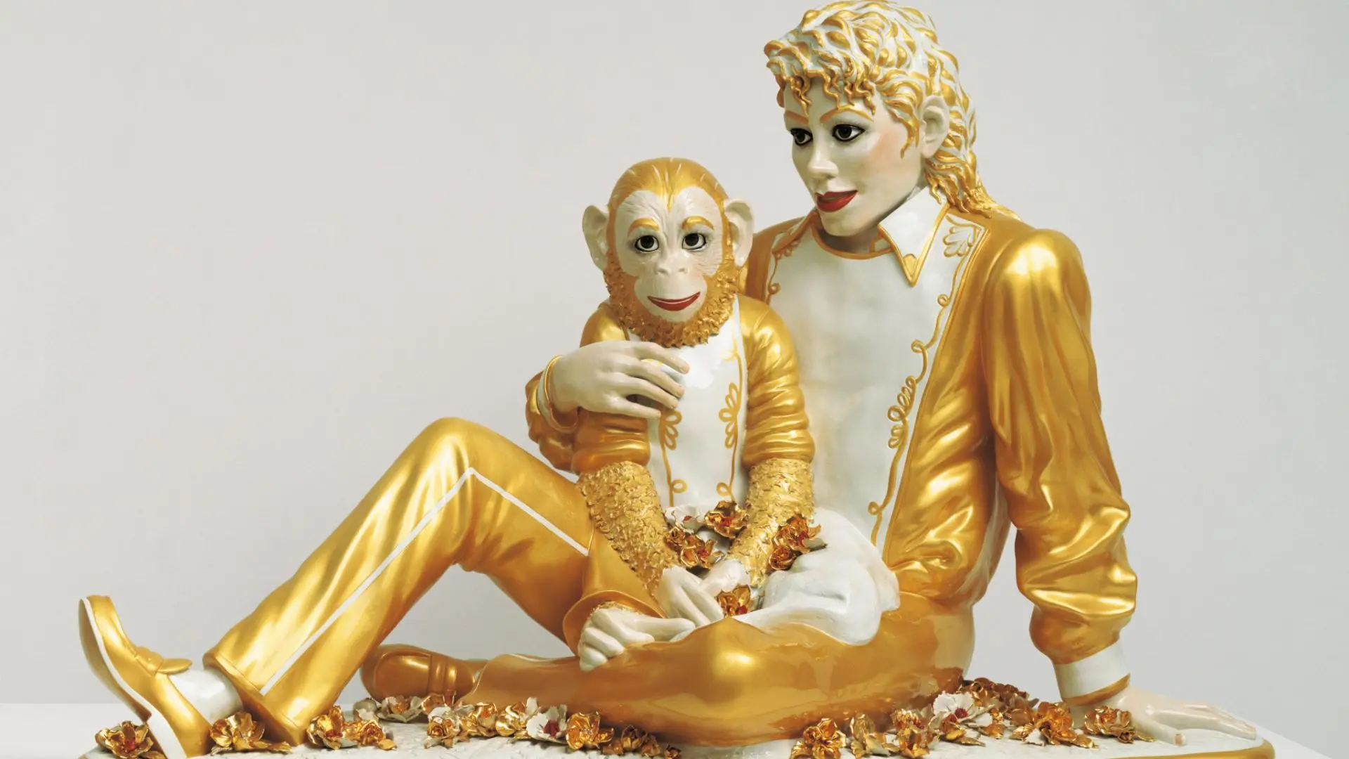 Golden sculpture featuring a seated michael jackson holding a monkey figure with detailed white and gold painted textures