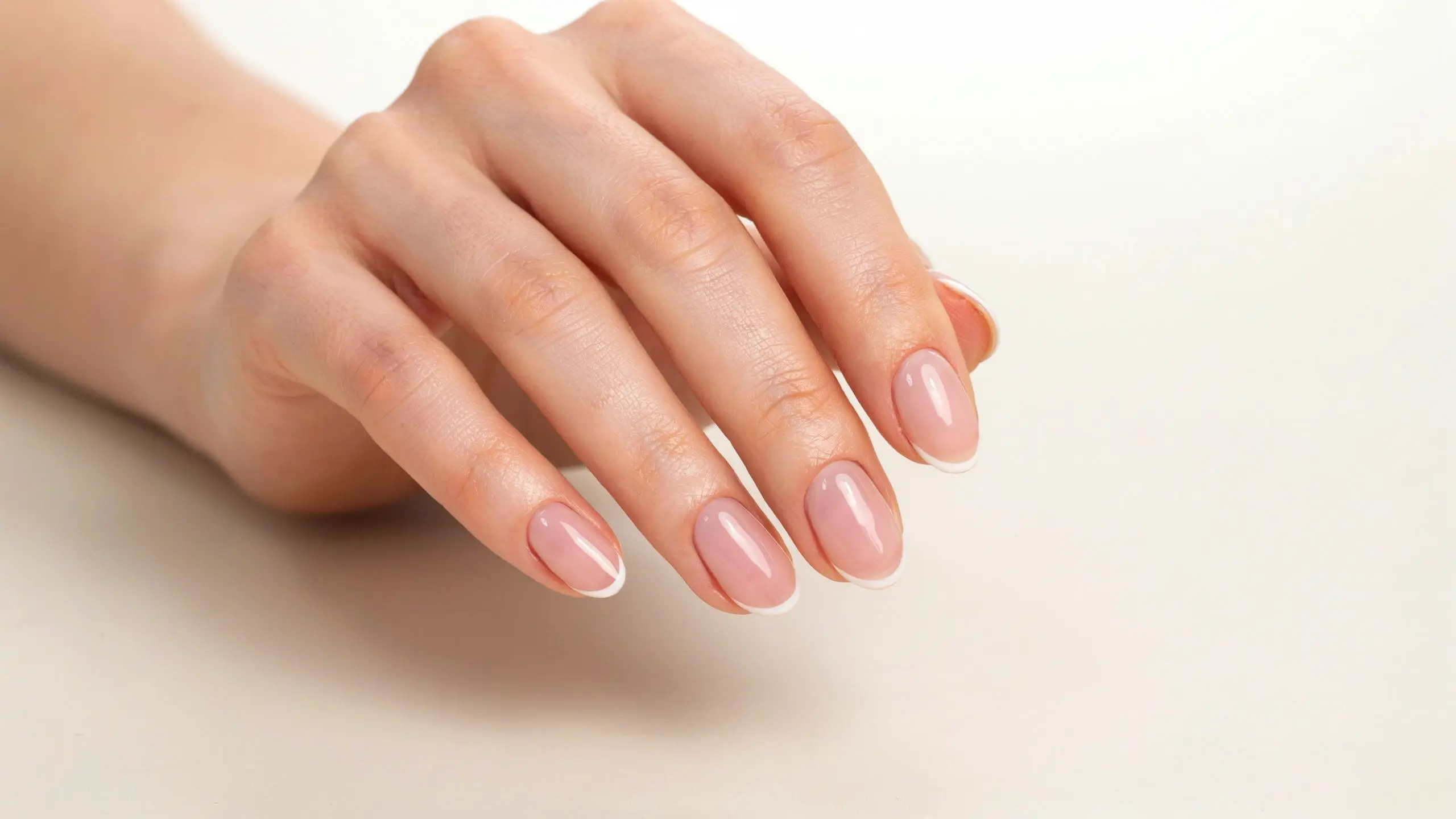 Hand showing micro French tip nails with delicate white edges and glossy nude polish on short rounded nails