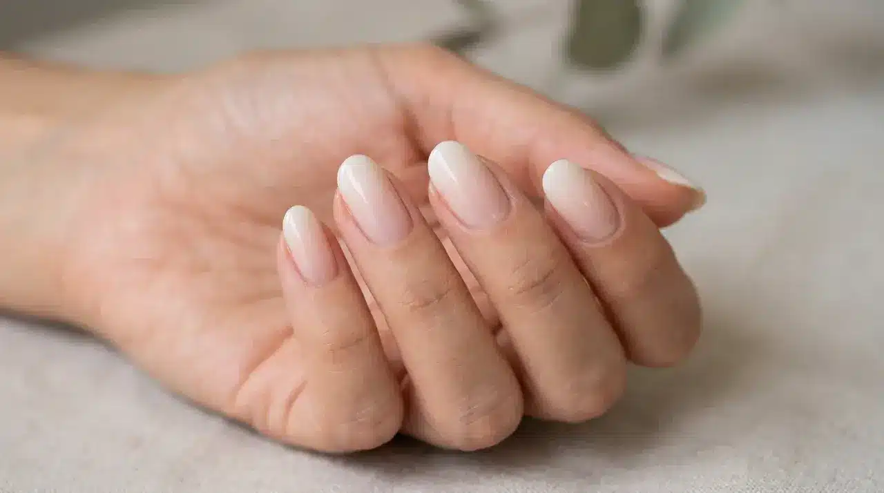 Close-up of almond shaped milky white nails with a sheer glossy finish on a hand resting on a soft neutral surface