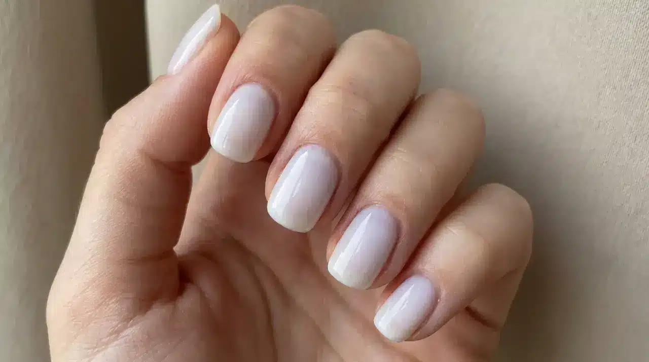 Short square milky white nails with a glossy sheer finish on a hand showing a clean minimalist manicure style