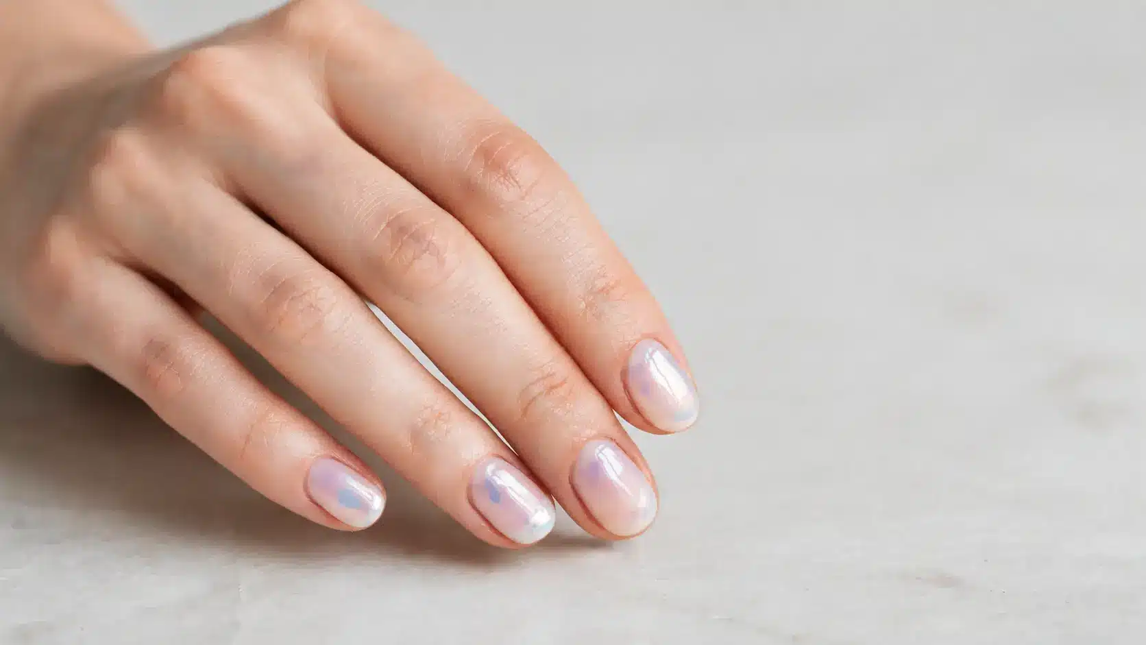 Hand with mother of pearl nails showing pearly shimmer finish and glossy polish in soft natural lighting