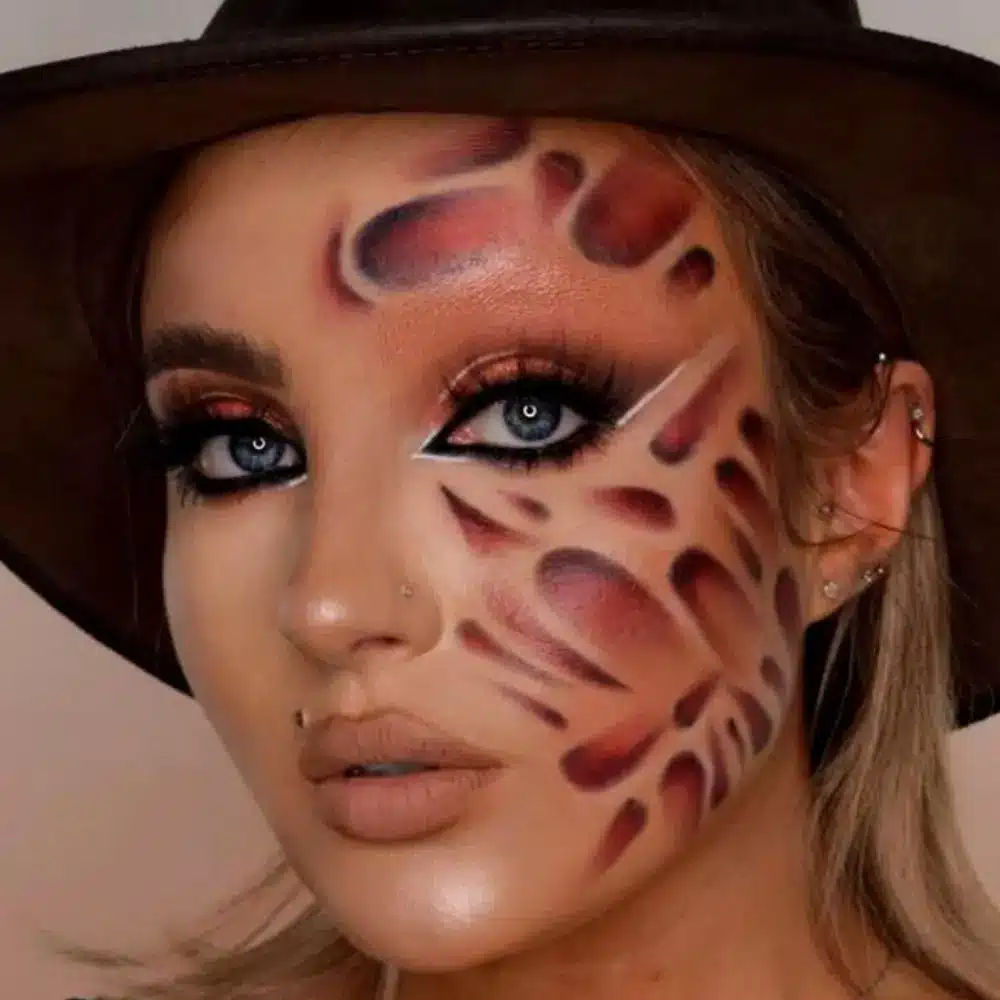 Mrs Krueger makeup with textured burn scars, mottled red and brown tones, smudged dark lips, and eerie skin details