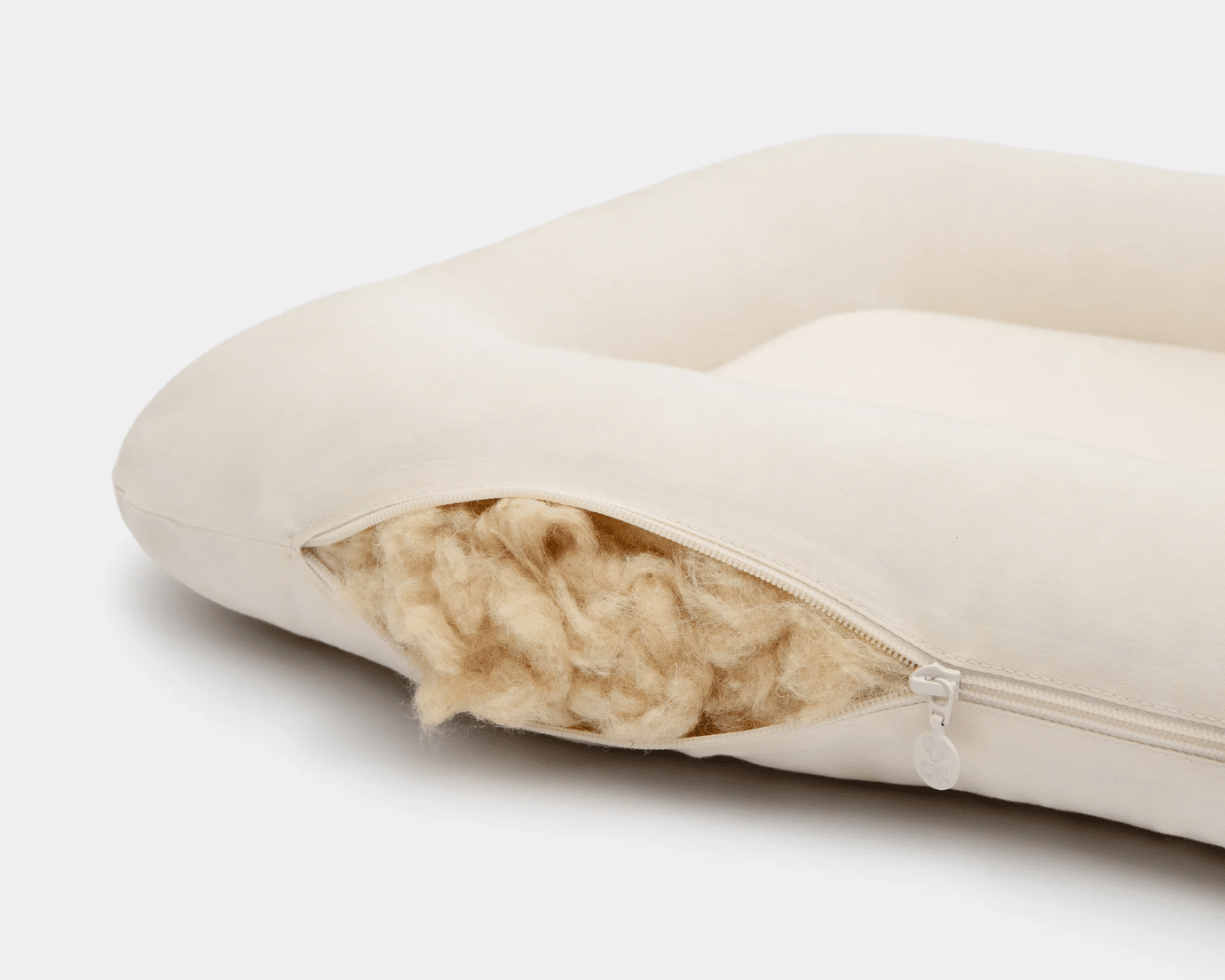 Cream-colored pet bed with open zipper revealing wool filling on white background