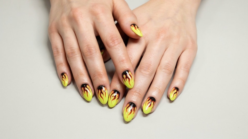 Neon yellow flame nails with bold black and orange tip designs and glossy finish