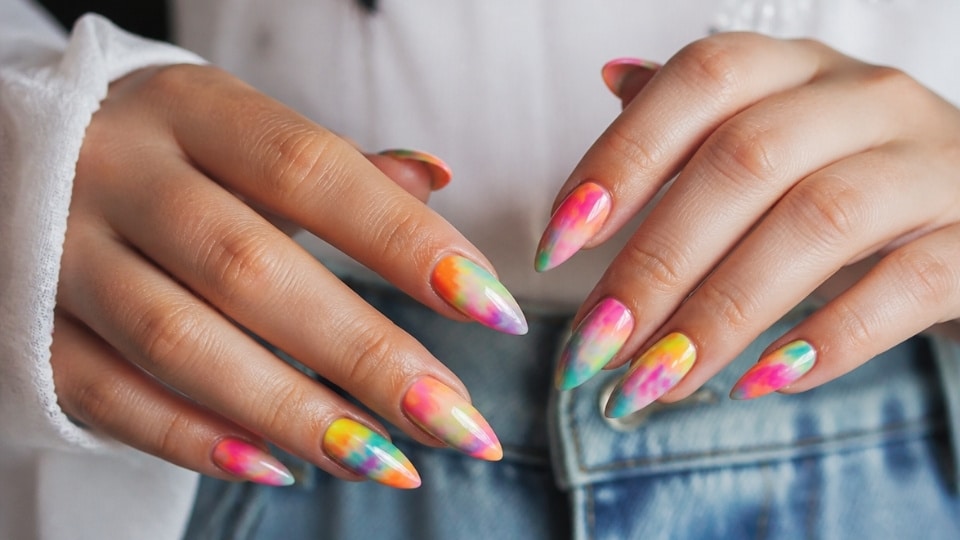 Neon tie dye nails blending pink orange yellow green and purple shades into a colorful swirl design