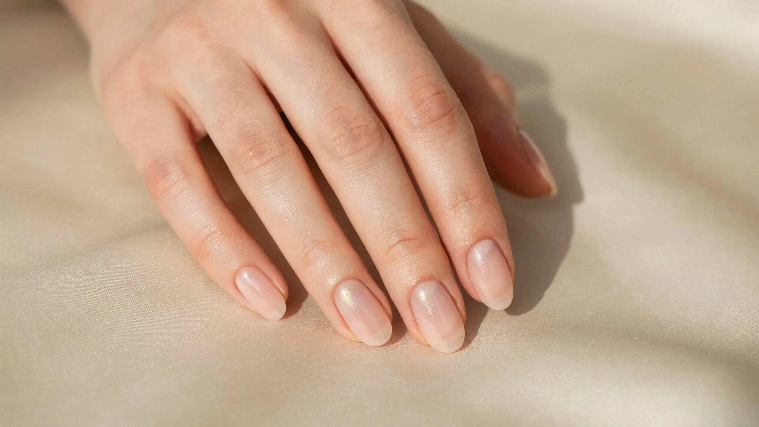Hand displaying neutral chrome nails with subtle reflective shine and soft nude tones on a clean surface