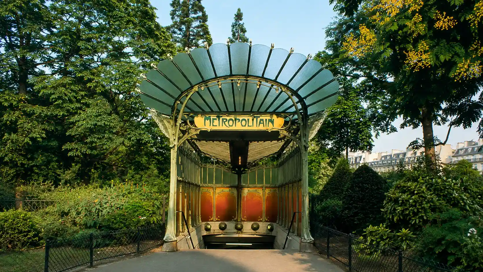 Historic Paris metro entrance with Art Nouveau iron canopy surrounded by green trees and garden plants