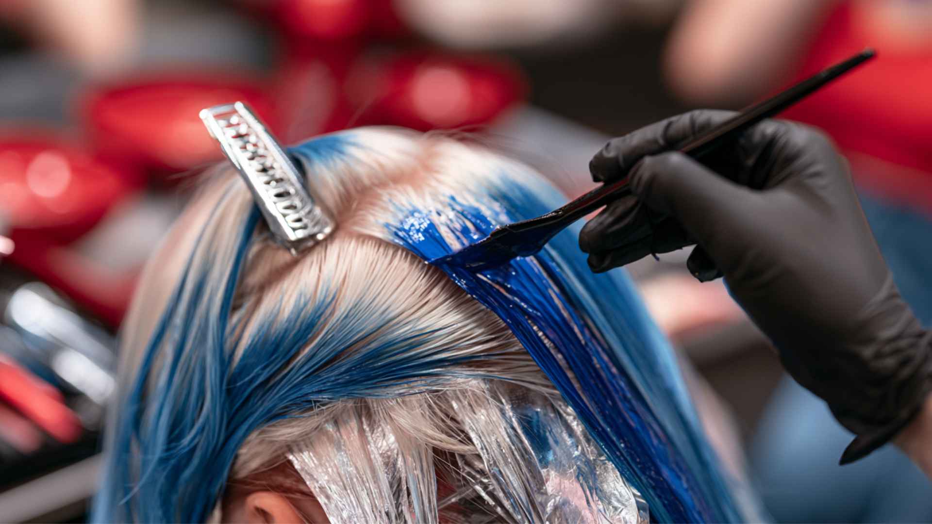Hair colorist applying blue permanent dye to sections of hair with a tint brush in a salon setting.