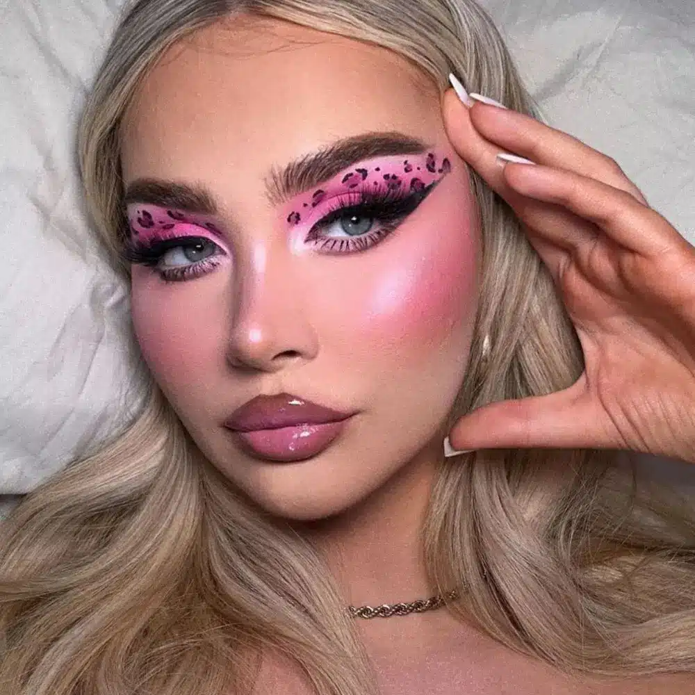 Pink leopard makeup with rosy eyeshadow, irregular black animal spots across eyes and cheek, and matching pink lips